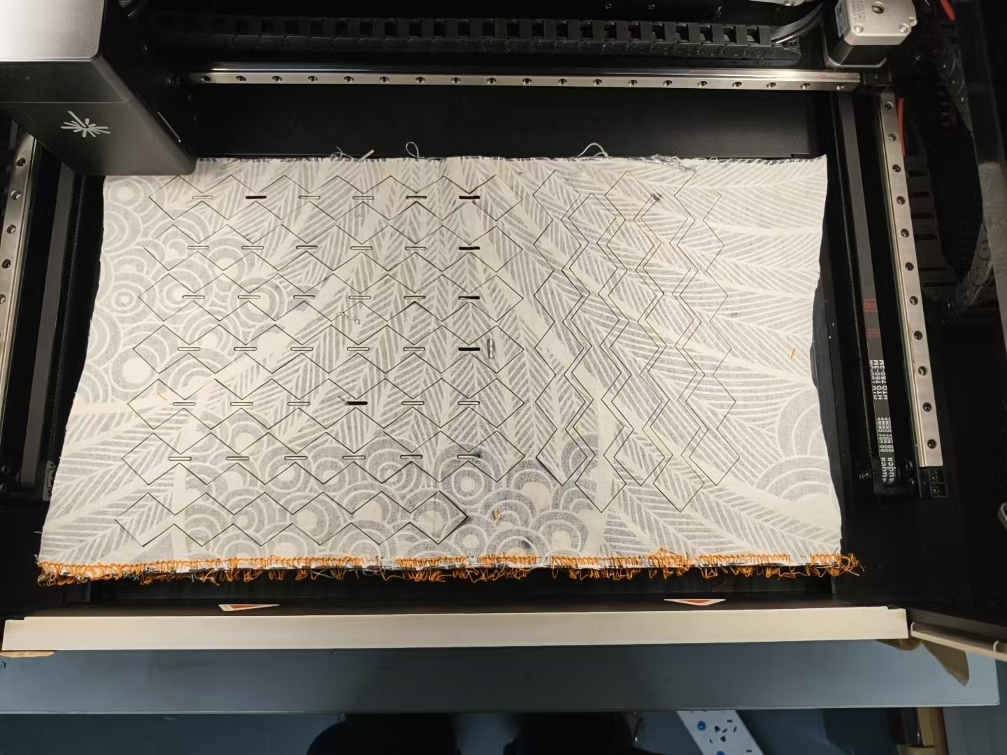 The cut sheet in the machine bed — outlines and slits cut through the printed cotton