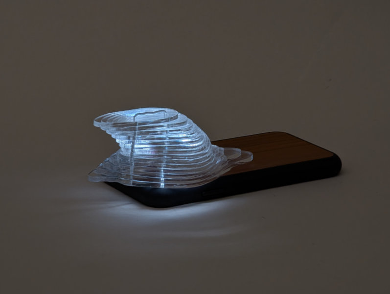 clear plastic form made of stacked layers lit below by phone flashlight