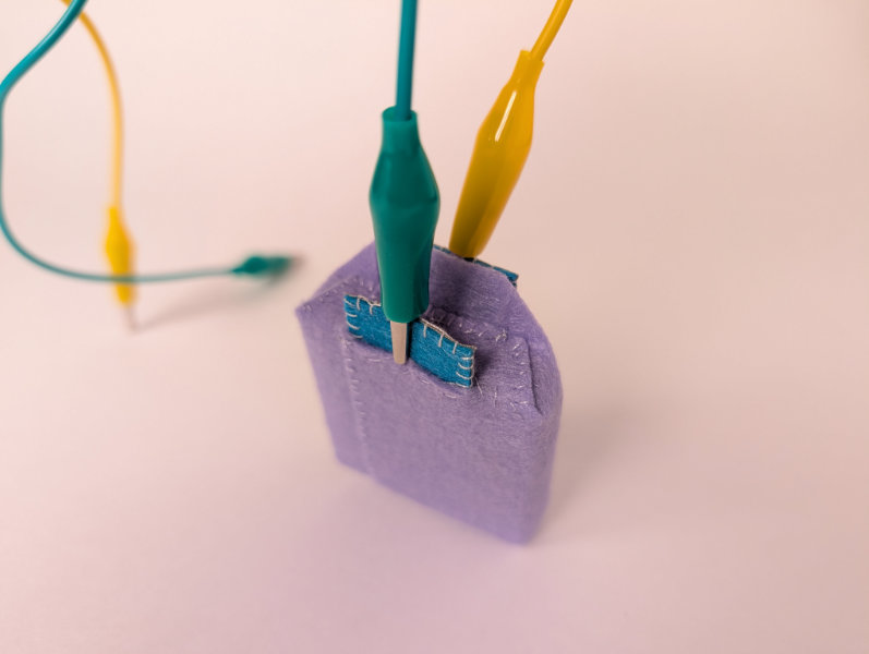 Purple felt box with green and yellow alligator clips attached to tabs