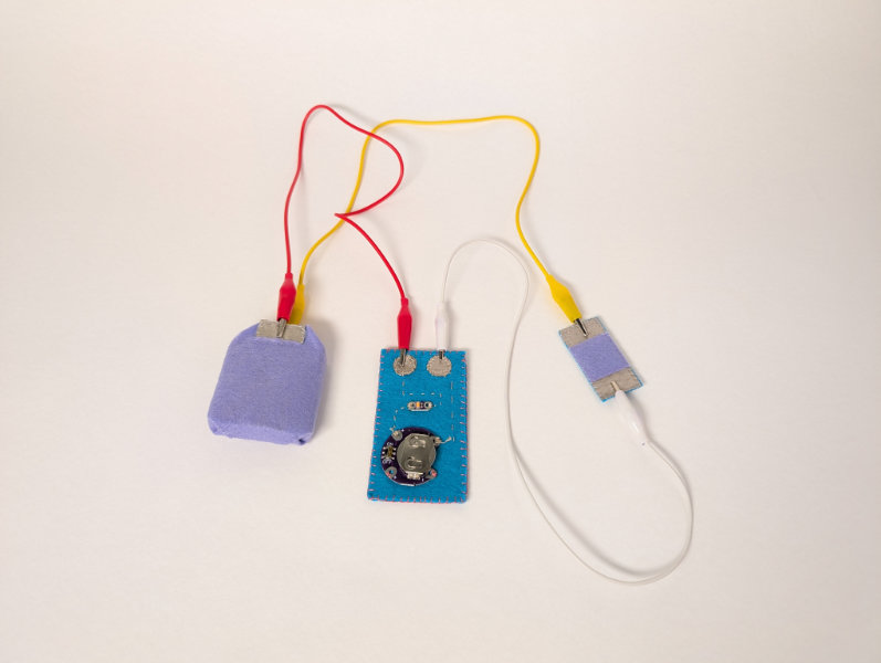 red, yellow, and white alligator clips connecting blue rectangle with battery and LED to purple felt box and purple/silver rectangular pad
