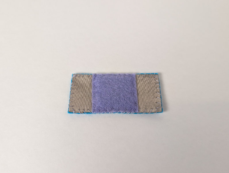 rectangle of felt with silver fabric pads on either end and a purple felt square in teh middle, all stitched together