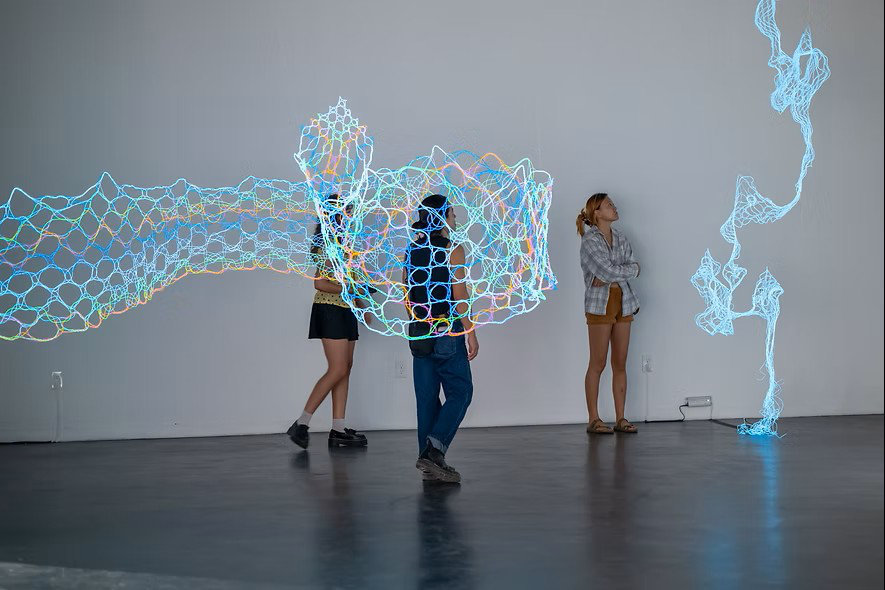 rainbow glowing lace and vertical blue glowing lace in front of people in a gray room