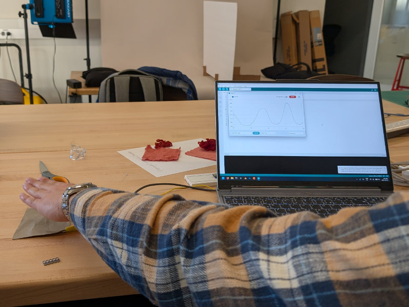 Photo of fab lab with person holding hand over silver fabric and laptop screen showing up and down curve graph