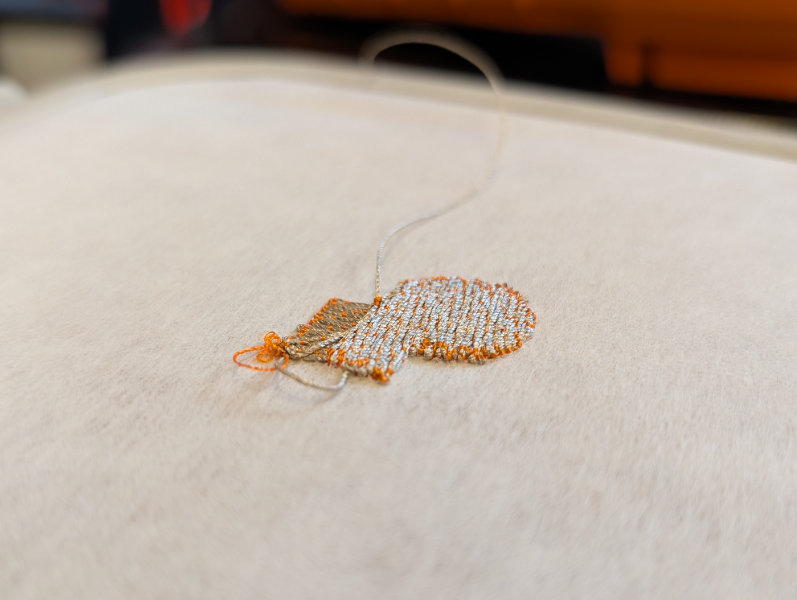 closeup of linen fabric with silver and orange thick embroidery patch