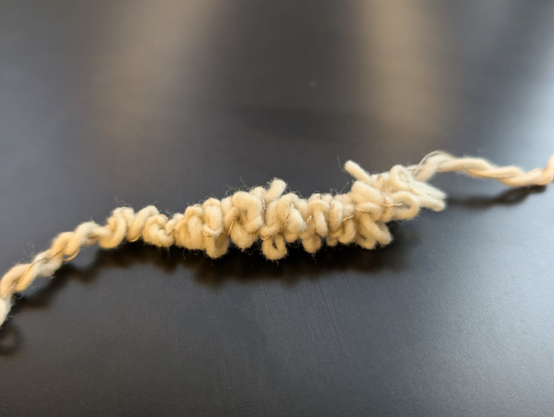 natural wool yarn bunched up on itself with silver thread woven in